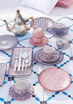 a table topped with plates and cups next to a tea pot on top of a tiled floor