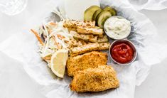 a white plate topped with chicken, coleslaw and cucumber wedges