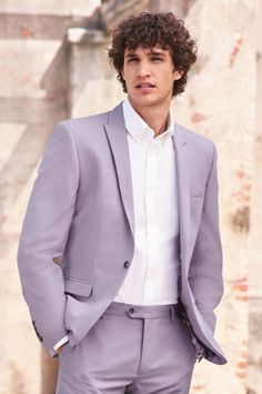 a man wearing a suit and tie standing in front of a wall with his hands in his pockets