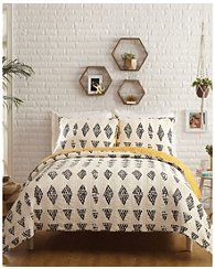 a bed with white and yellow bedspread in front of a brick wall next to potted plants