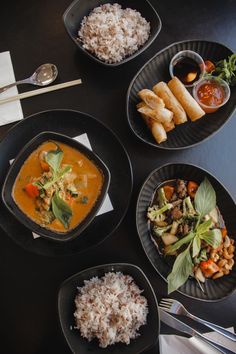 four black plates filled with food on top of a table next to silverware and utensils