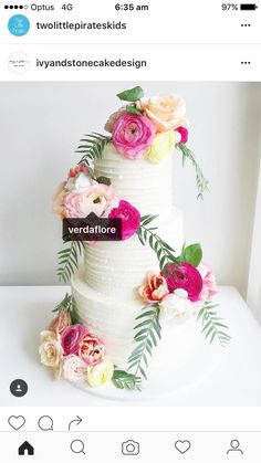 a white wedding cake with pink and yellow flowers on the top tier, surrounded by greenery