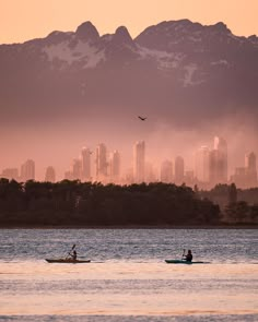 two people are in small boats on the water with mountains in the backgroud