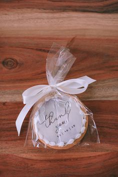 a cookie wrapped in clear cellophane and tied with a white ribbon on top of a wooden table