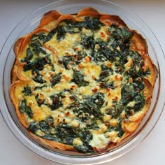 a quiche with spinach and cheese in a glass dish on a white table