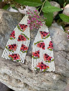 two pairs of beaded earrings sitting on top of a rock next to some flowers