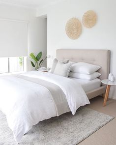 a bed with white linens and pillows in a bedroom next to a plant on the wall