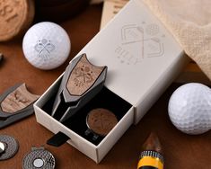 two wooden golf ball markers in a box next to some golf balls and tees