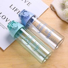 two water bottles sitting next to each other on top of a wooden table with a book in the background