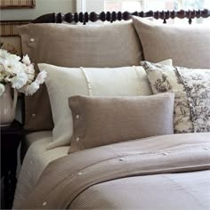 a bed topped with lots of pillows next to a vase filled with flowers on top of it