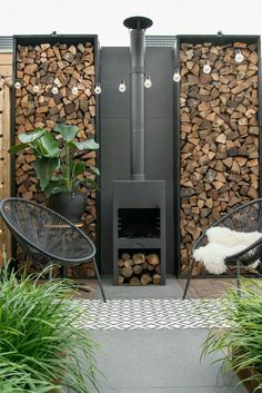 an outdoor fire place surrounded by plants and wood stacked on top of eachother