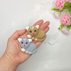 a hand holding two small crocheted animals on it's fingers next to pink flowers