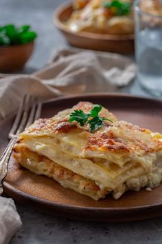 a plate topped with lasagna covered in cheese and parsley next to a glass of water