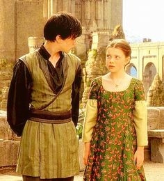 the young man and woman are dressed in medieval clothing, standing next to each other