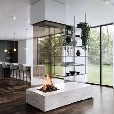 a modern fireplace in the middle of a living room with glass walls and floor to ceiling windows