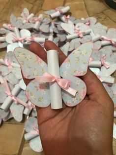 a hand holding a small white tube with pink bows on it and lots of paper flowers in the background