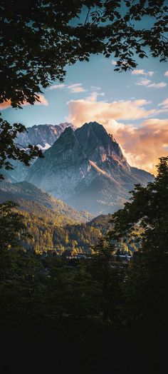 the mountains are covered in trees and clouds as the sun is setting on top of them