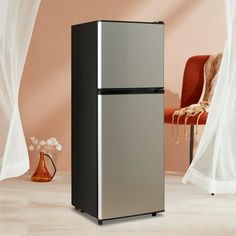 a silver and black refrigerator sitting in front of a red chair next to a white curtain