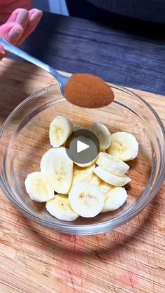 someone is cutting bananas into small pieces in a glass bowl on a wooden table with a spoon