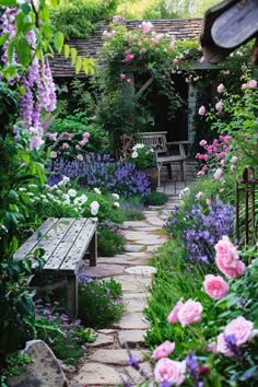 a garden with pink and purple flowers, benches and stone path leading to the house