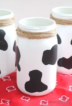 three mason jars decorated with black and white cow prints on red tablecloth, one is empty