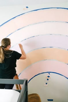 a woman is painting a wall with blue and pink stripes on it's walls