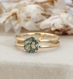 two gold rings with a green stone in the middle and white flowers in the background