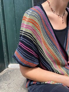 a woman sitting on the ground wearing a multicolored knitted sweater and necklace