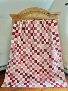 a red and white checkered quilt on a wooden headboard in a room with hardwood floors