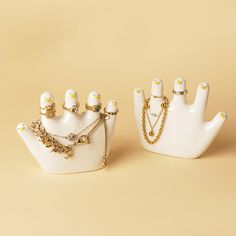 two white hand shaped objects with gold chains on them, one holding a necklace and the other wearing a ring