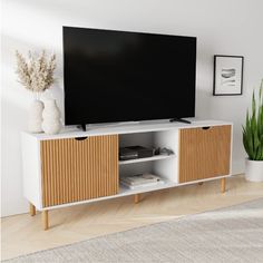 a flat screen tv sitting on top of a white entertainment center next to a potted plant