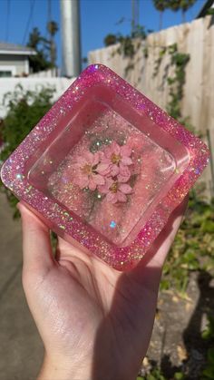 a hand holding up a pink square object with flowers on the inside and glitter in the outside