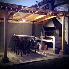 an outdoor kitchen is lit up at night with string lights on the ceiling and bar stools