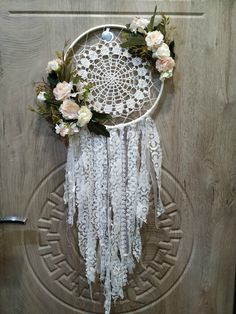 a white dream catcher hanging on a wooden door with flowers and leaves around the rim