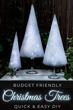 three white christmas trees sitting on top of a wooden table next to a sign that says budget friendly christmas trees quick and easy diy