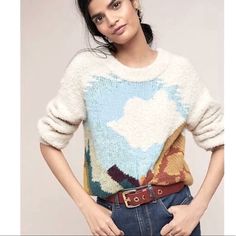 a woman is wearing a colorful sweater with clouds on it and a belt around her waist