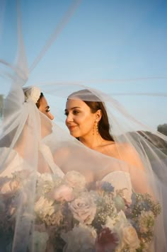 two women in wedding dresses are looking at each other with veils over their heads