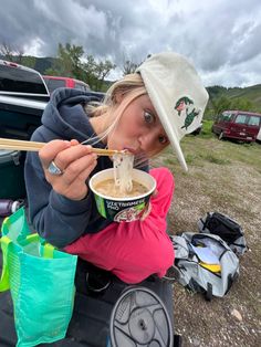 a woman eating noodles from a bowl with chopsticks in her hand while camping