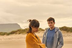 a man standing next to a woman on top of a beach