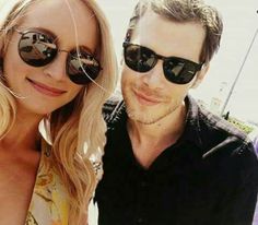 a man and woman wearing sunglasses pose for a photo together in front of a building