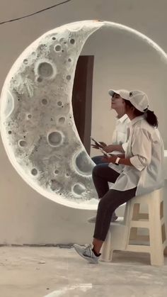 a woman sitting on top of a white chair next to a moon shaped object with holes in it