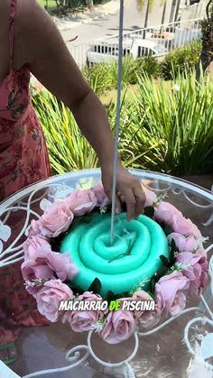 a woman is decorating a cake with blue icing and pink flowers on it