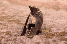 a helmet is laying on the ground in front of some grass and dirt, it looks like an old roman soldier's helmet