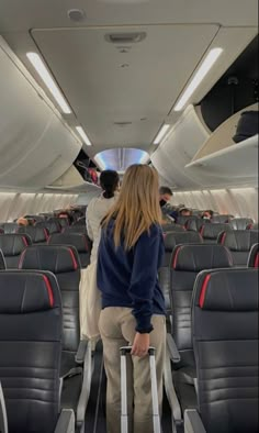 a woman is standing on an airplane with her luggage and looking out the window at other passengers