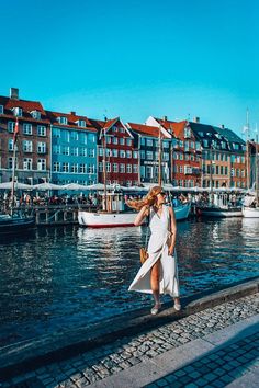 a woman standing on the side of a river in front of some buildings and boats