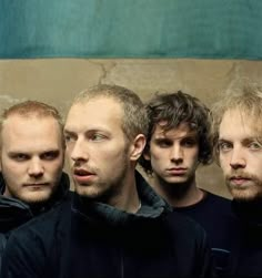 four men standing next to each other in front of a wall