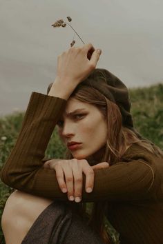 a woman sitting in the grass with her hands on her head and looking off into the distance