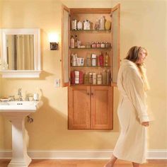 a woman in a bathrobe standing next to a bathroom sink and medicine cabinet