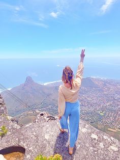 a woman standing on top of a rock with her arms in the air