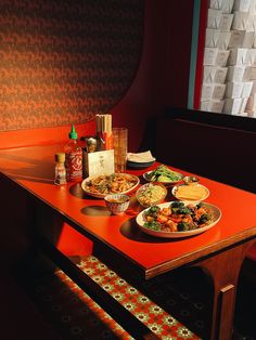 an orange table topped with plates of food and condiments next to a window